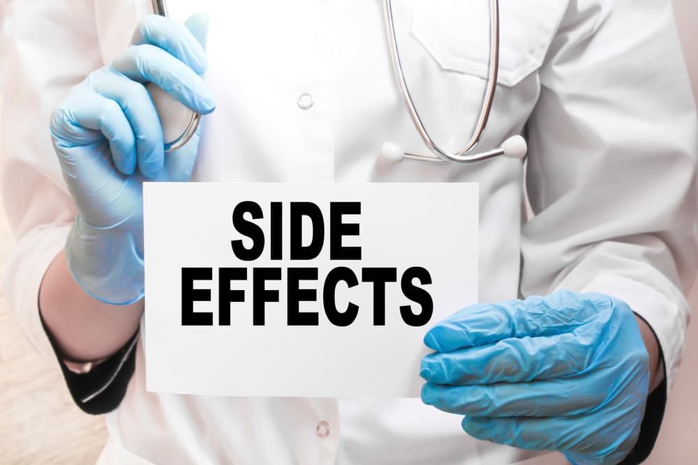 The doctor's blue-gloved hands display the word "SIDE EFFECTS" on a white background. Medical concept.