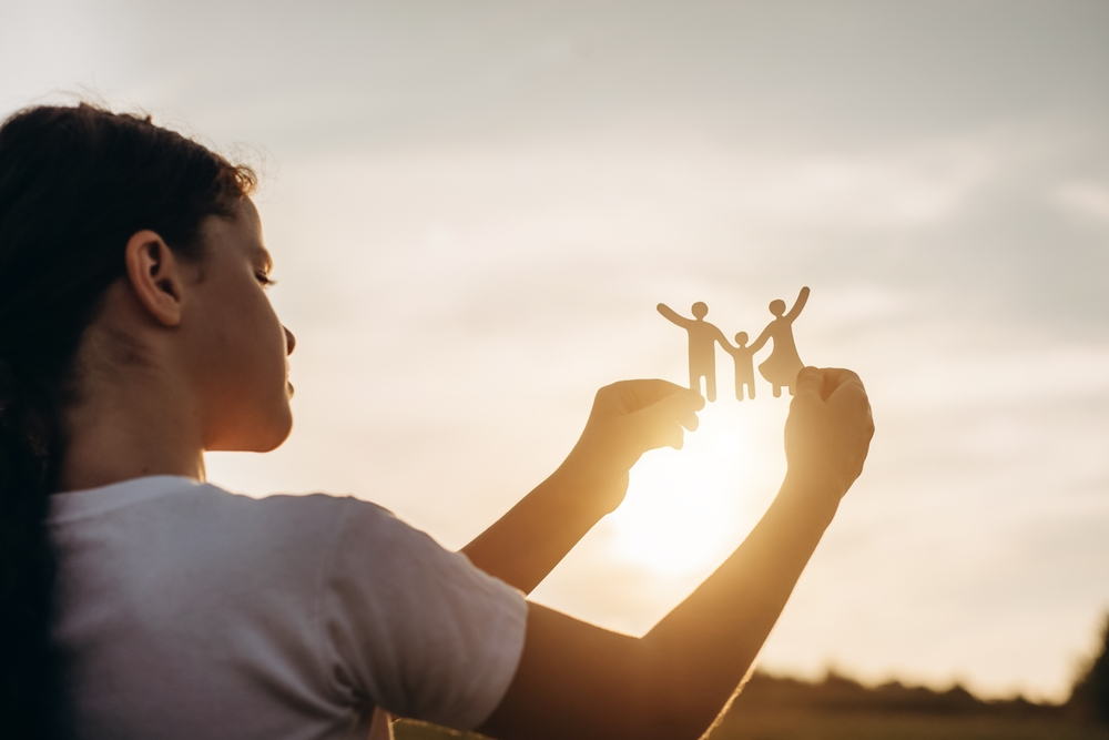 teen girl hold paper cutout of a family up to sunlight to represent her desire for a family of her own