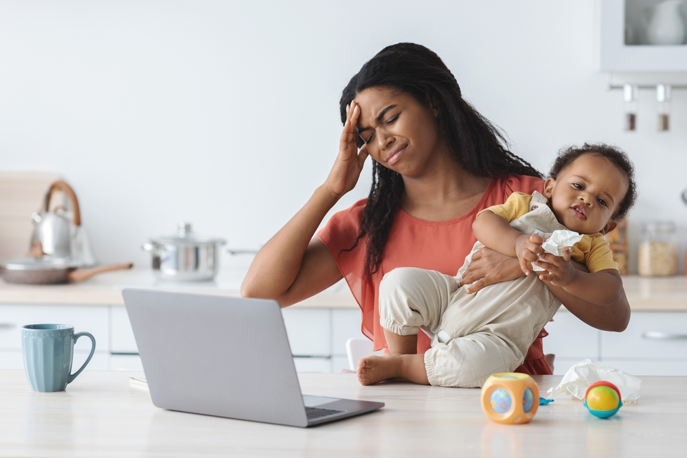 A concerned mother holding her baby while looking at a laptop, representing the emotional burden and legal research involved for families affected by Neocate-related injuries.